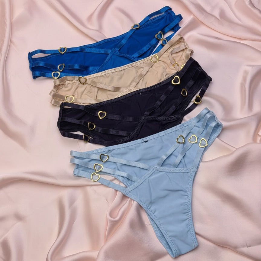 Four pairs of lingerie with heart-shaped grommets on a pink fabric background.