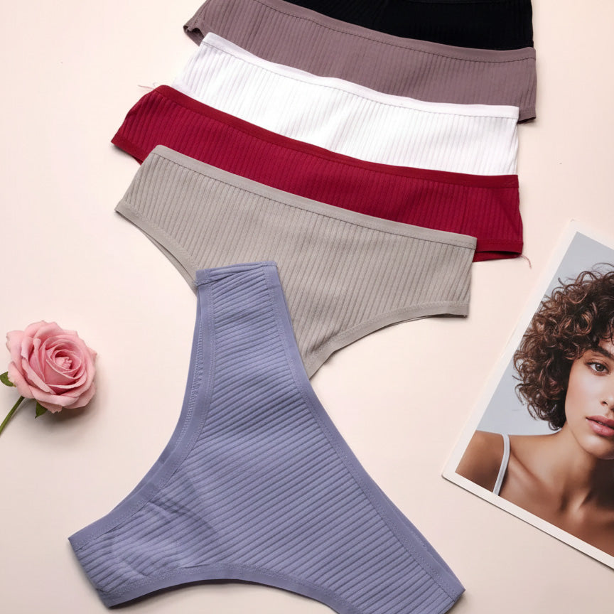Four pairs of women's underwear in different colors on a light background with a magazine and rose.
